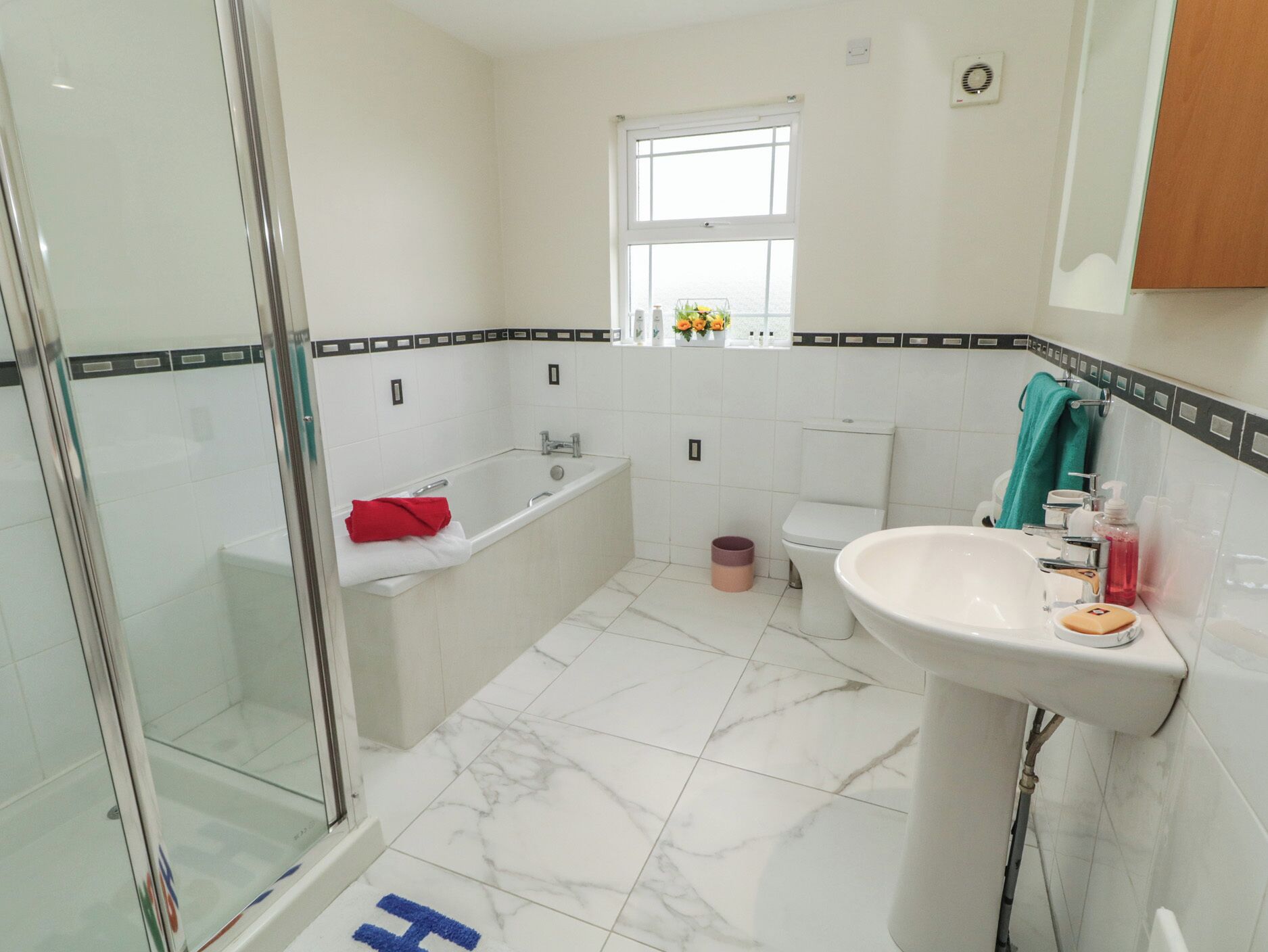 A bathroom with a glass shower enclosure, a bathtub, a toilet, and a sink.