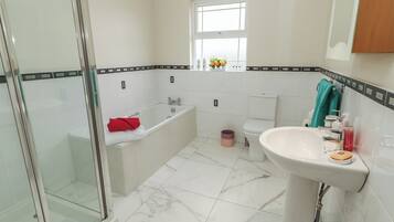 A bathroom with a glass shower enclosure, a bathtub, a toilet, and a sink.