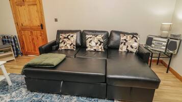 A black leather sectional sofa with patterned cushions, a small glass table with a radio and speakers, and a wooden door in the background.