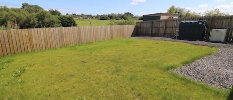 A fenced backyard with a grassy area, a wooden structure, and a gravel path.