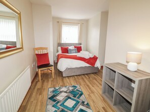 A bedroom with a bed, a chair, a bedside table with a lamp, and a patterned rug. - The Sperrin Getaway (Omagh)