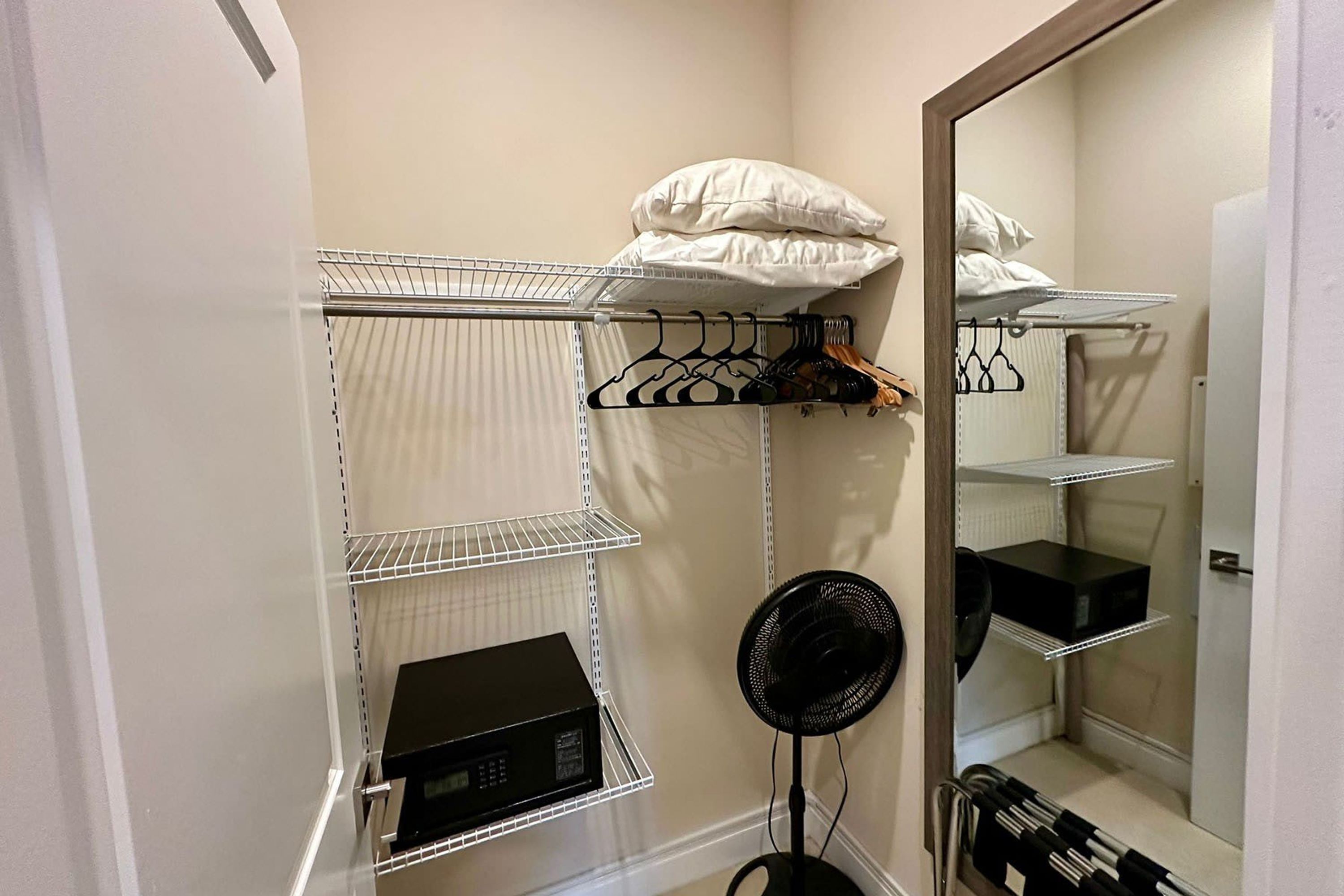 Un placard avec des étagères, un ventilateur et une tringle pour suspendre les vêtements.