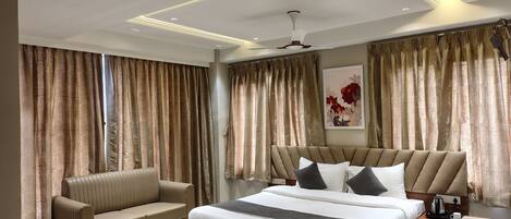 A modern hotel room with a large bed, a sofa, a desk, and curtains.