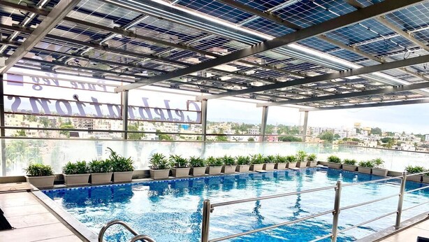 A rooftop swimming pool with a view of the cityscape, surrounded by potted plants and equipped with metal railings. - Rudanta Regency  (Phaltan)