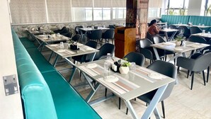 A restaurant with long communal tables, individual booths, and a high ceiling. - Rudanta Regency  (Phaltan)