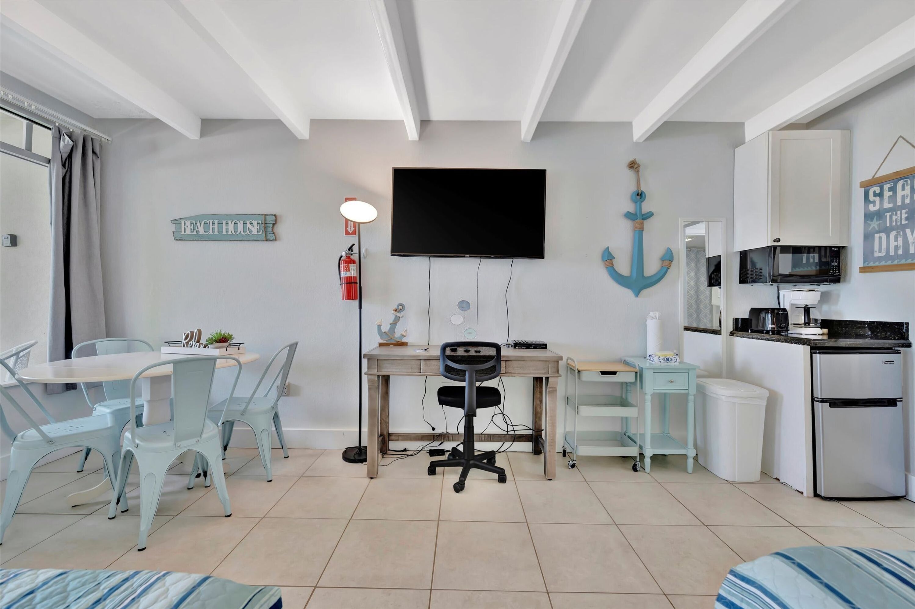 A modern kitchen with a microwave, stove, and refrigerator. There is a dining area with a table and chairs, and a TV mounted on the wall.