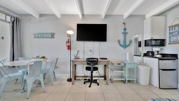 A modern kitchen with a microwave, stove, and refrigerator. There is a dining area with a table and chairs, and a TV mounted on the wall.