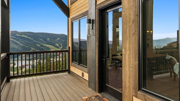 A wooden deck with a glass door leading to a room, overlooking a valley.
