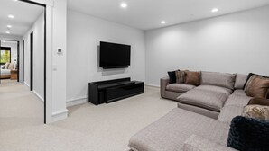 A modern living room with a large sectional sofa, a flat-screen TV mounted on the wall, and a black entertainment unit.