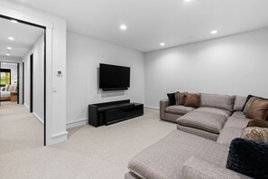 Una sala de estar moderna con un sofá seccional grande, un televisor de pantalla plana montado en la pared y un mueble de entretenimiento negro.