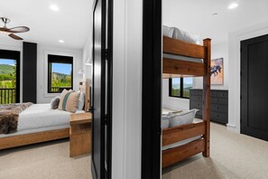 A bedroom with two bunk beds, a ceiling fan, a dresser, and a window with a view of greenery. - Lavish 6 Bedroom Ski Accessible Home (Big Sky)