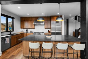 A modern kitchen with wooden cabinets, a large island with bar stools, stainless steel appliances, and pendant lighting.