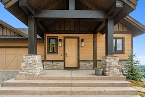 A wooden house with a stone entrance, a garage, and a view of the mountains. - Lavish 6 Bedroom Ski Accessible Home (Big Sky)