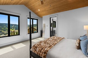 Un dormitorio con un ventanal grande, una cama con una manta de piel sintética y techo de madera.