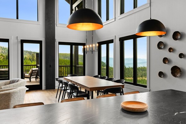 A modern dining area with a large table, chairs, and pendant lights.