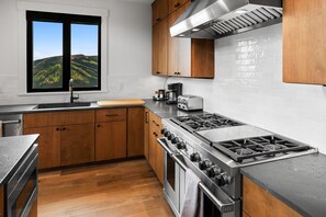 A modern kitchen with wooden cabinets, a stainless steel stove, and a window with a view of hills.