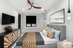 Quarto moderno com cama, mesa de cabeceira e ventilador de teto.