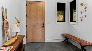 A modern interior with a wooden door, a bench, a small table with a lamp, and wall-mounted animal head decorations. - Lavish 6 Bedroom Ski Accessible Home (Big Sky)