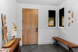 A modern interior with a wooden door, a bench, a small table with a lamp, and wall-mounted animal head decorations. - Lavish 6 Bedroom Ski Accessible Home (Big Sky)
