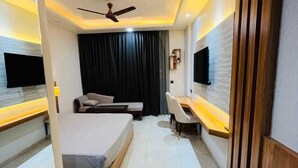 A modern hotel room with a bed, a desk, a chair, a TV, and a ceiling fan.