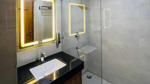 A modern bathroom with a black countertop, two sinks, a large mirror with illuminated edges, and a glass-enclosed shower area.