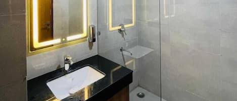 Ein modernes Badezimmer mit schwarzem Waschtisch, zwei Waschbecken, einem großen Spiegel mit beleuchtetem Rand und einer Duschkabine aus Glas.
