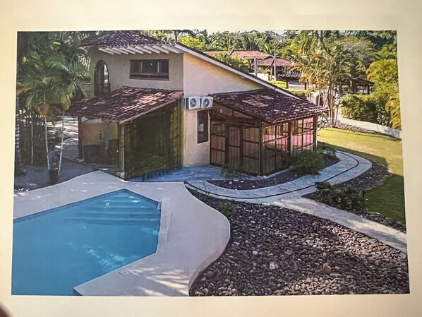 Une maison avec une piscine, un patio couvert et un jardin.