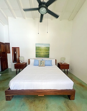 Een slaapkamer met een houten bed, twee nachtkastjes met lampen, een plafondventilator en een schilderij aan de muur.