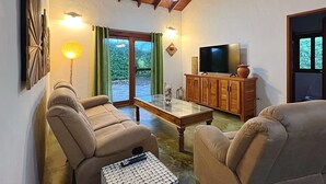 Een woonkamer met twee beige banken, een glazen salontafel, een televisie op een houten kast en een plafondventilator.