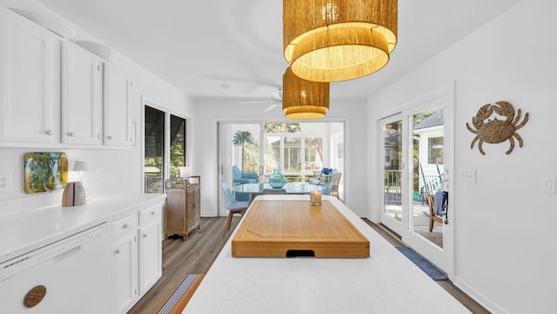 A modern kitchen with white cabinetry, a wooden dining table, and a large window.