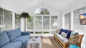 A sunlit room with a blue sofa, a wicker chair, and a small table.