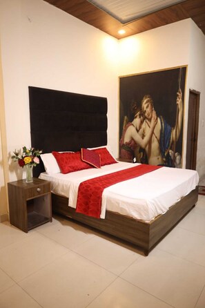 A bedroom with a large bed, a nightstand with a vase of flowers, and a painting on the wall. - Hotel Haveli Inn (Varanasi)