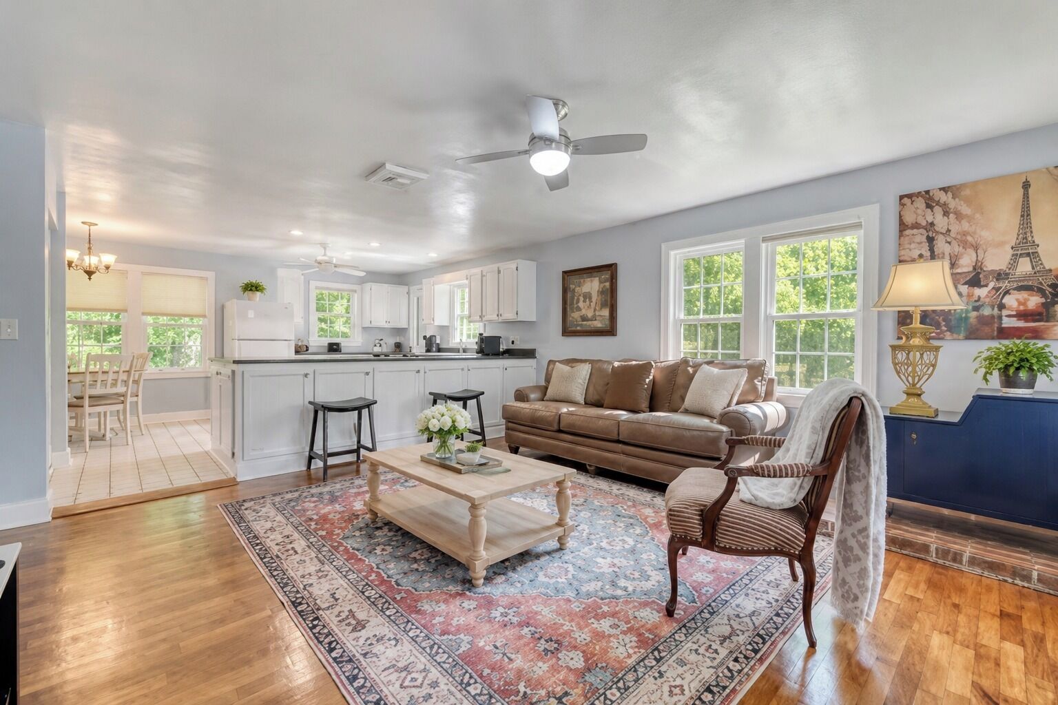 A spacious living room with a large window, a ceiling fan, and a dining area with a view of the kitchen.