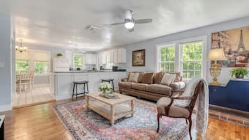 A spacious living room with a large window, a ceiling fan, and a dining area with a view of the kitchen.