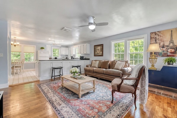 A spacious living room with a large window, a ceiling fan, and a dining area with a view of the kitchen.