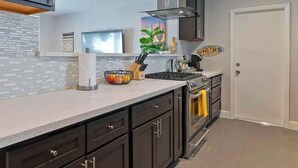 A modern kitchen with dark cabinetry, a stainless steel stove, and a tiled backsplash. - Palm Springs Oasis w/ Pool & Spa (Palm Springs)