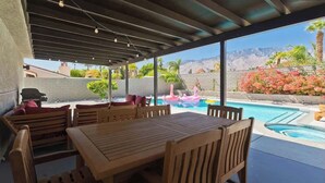 A covered outdoor area with a pool, wooden furniture, and a view of mountains and flowers. - Palm Springs Oasis w/ Pool & Spa (Palm Springs)