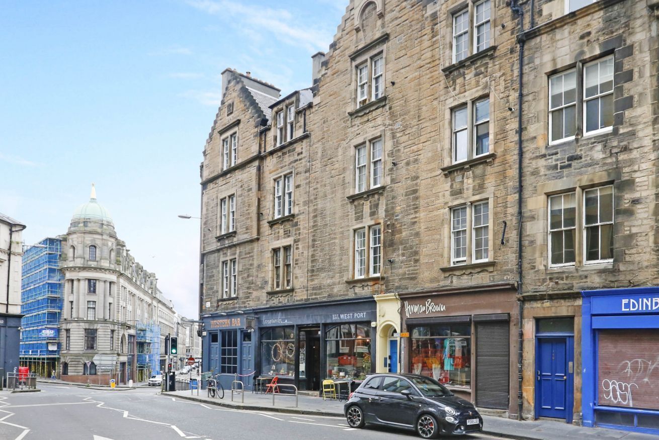 A street view with historic stone buildings, a dome structure, and various storefronts including a bar and a clothing store.
