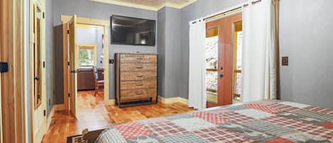 Un dormitorio con suelo de madera, una cama con colcha estampada, un aparador y un televisor en la pared.