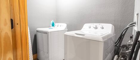 A laundry room with two white washing machines and a dryer, a wooden door, and a tiled floor.
