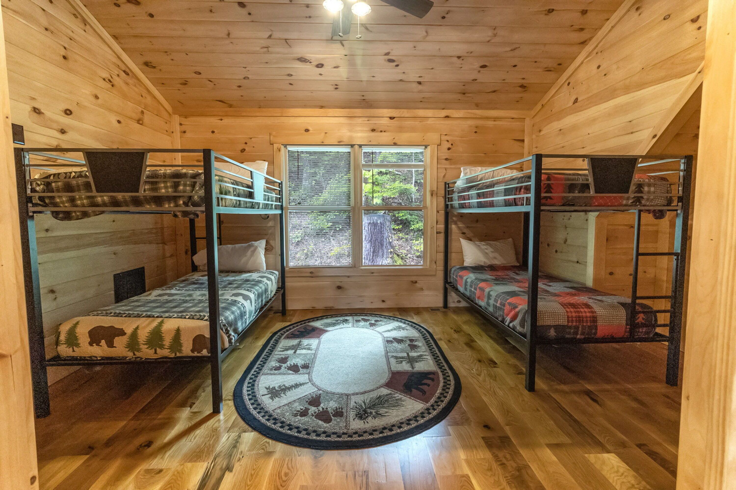 A cabin with three bunk beds, a large window with a view of trees, and a wooden floor.