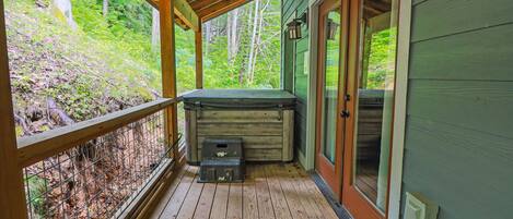Una terraza de madera con un jacuzzi, un área techada y vistas a un bosque.
