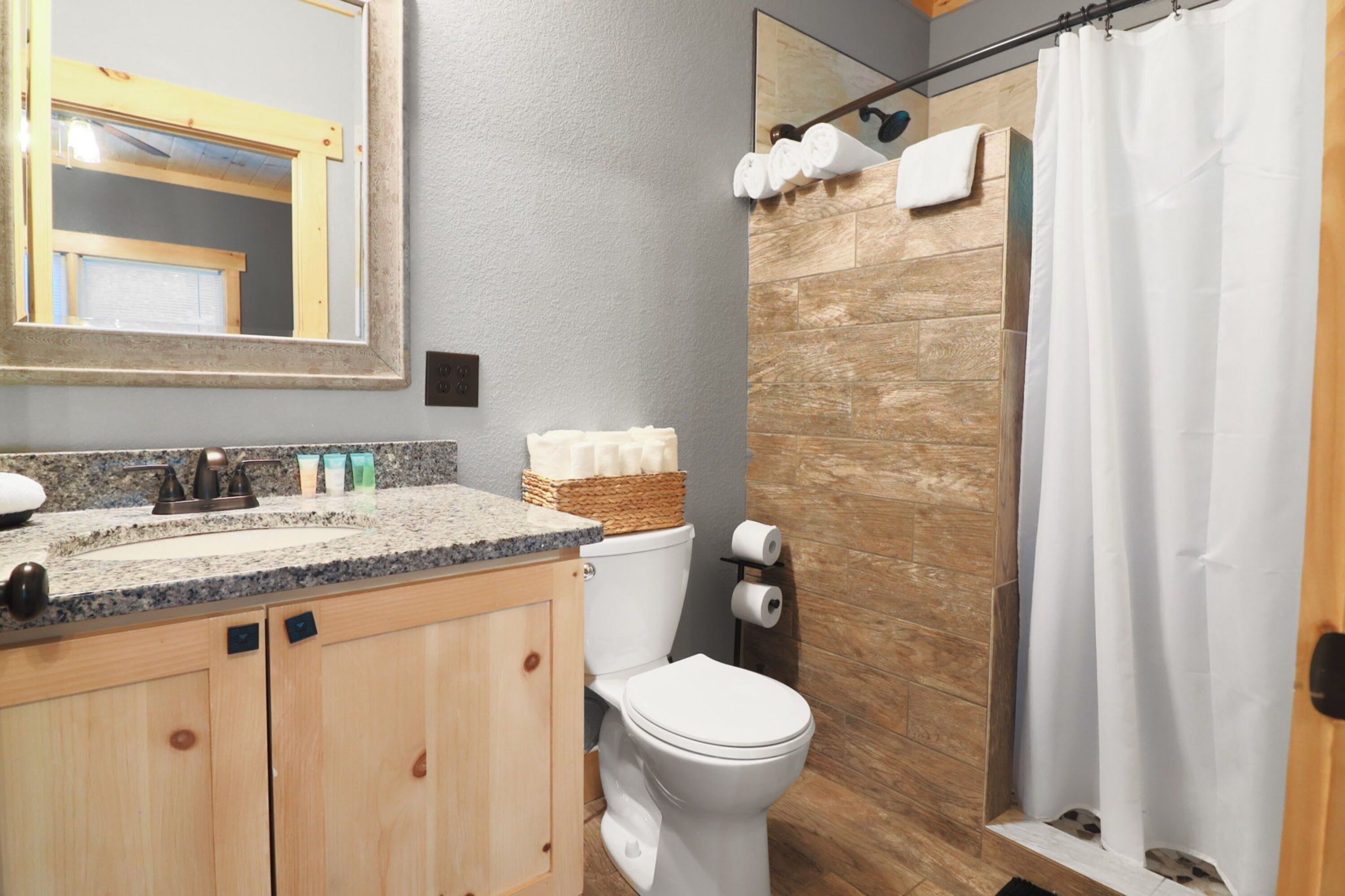 A bathroom with a wooden vanity, a toilet, and a shower with a curtain.