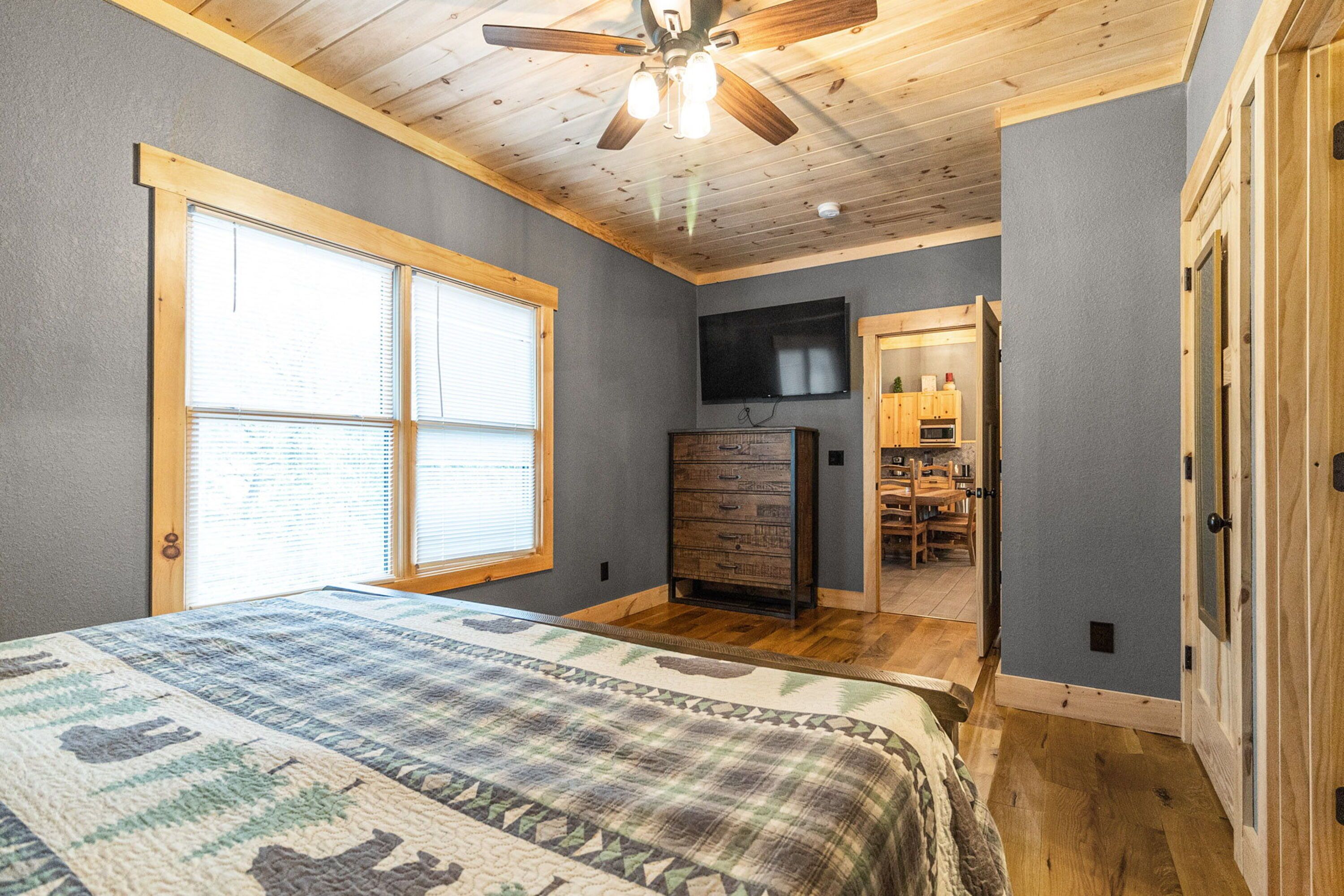 A bedroom with a large bed, wooden ceiling, and a TV mounted on the wall.