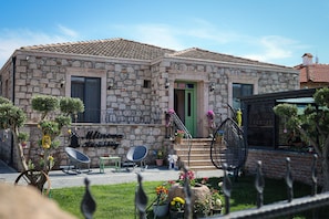 A stone building with a green door, a staircase, and a small garden with potted plants and a chair.