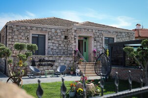 A stone building with a green door, a staircase, and a small garden with potted plants and a chair.