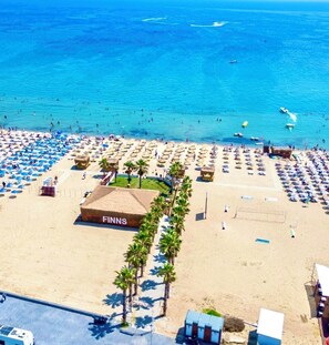 A beach with a large building labeled 'FINNS' and numerous umbrellas. - Mlinova Küçükköy (Ayvalık)