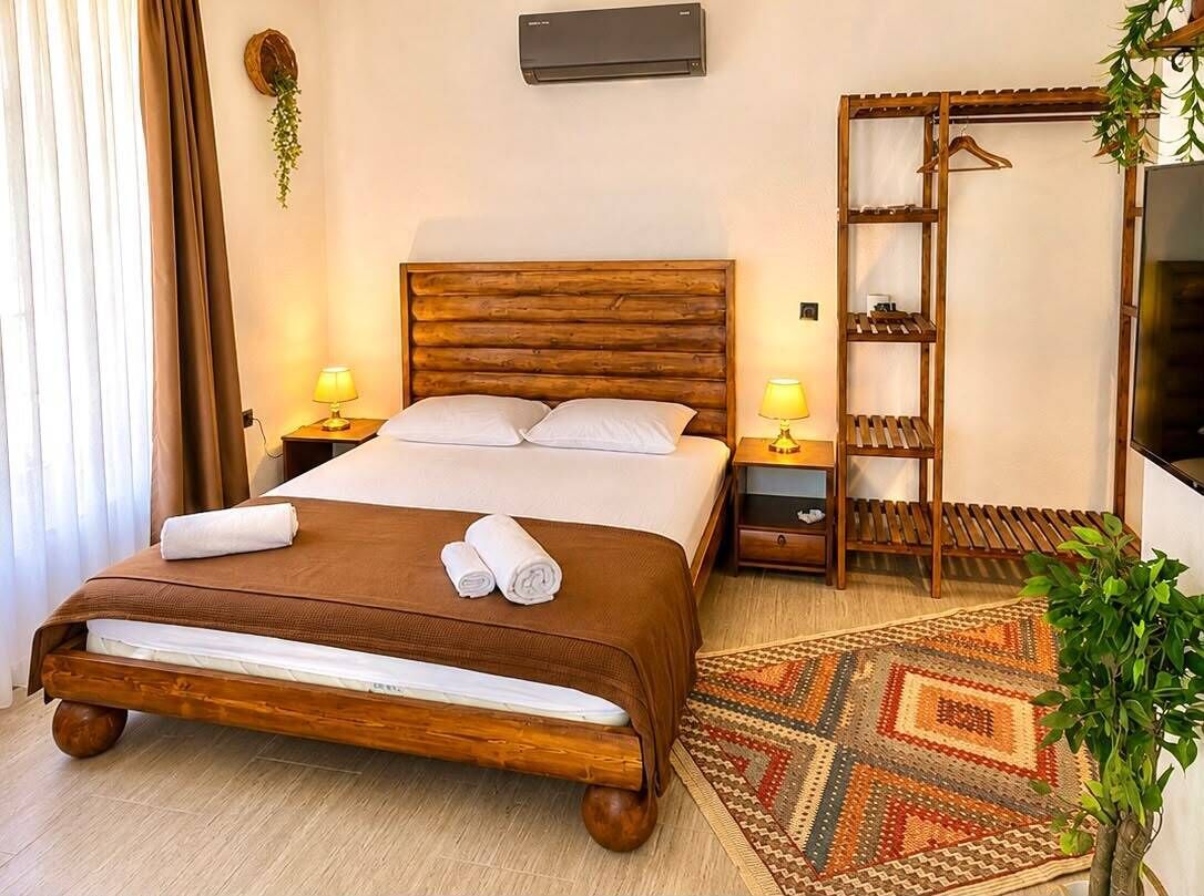 Una habitación de hotel con una cama de madera, dos lámparas de noche, un televisor, un armario y una alfombra estampada.