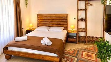 Una habitación de hotel con una cama de madera, dos lámparas de noche, un televisor, un armario y una alfombra estampada.