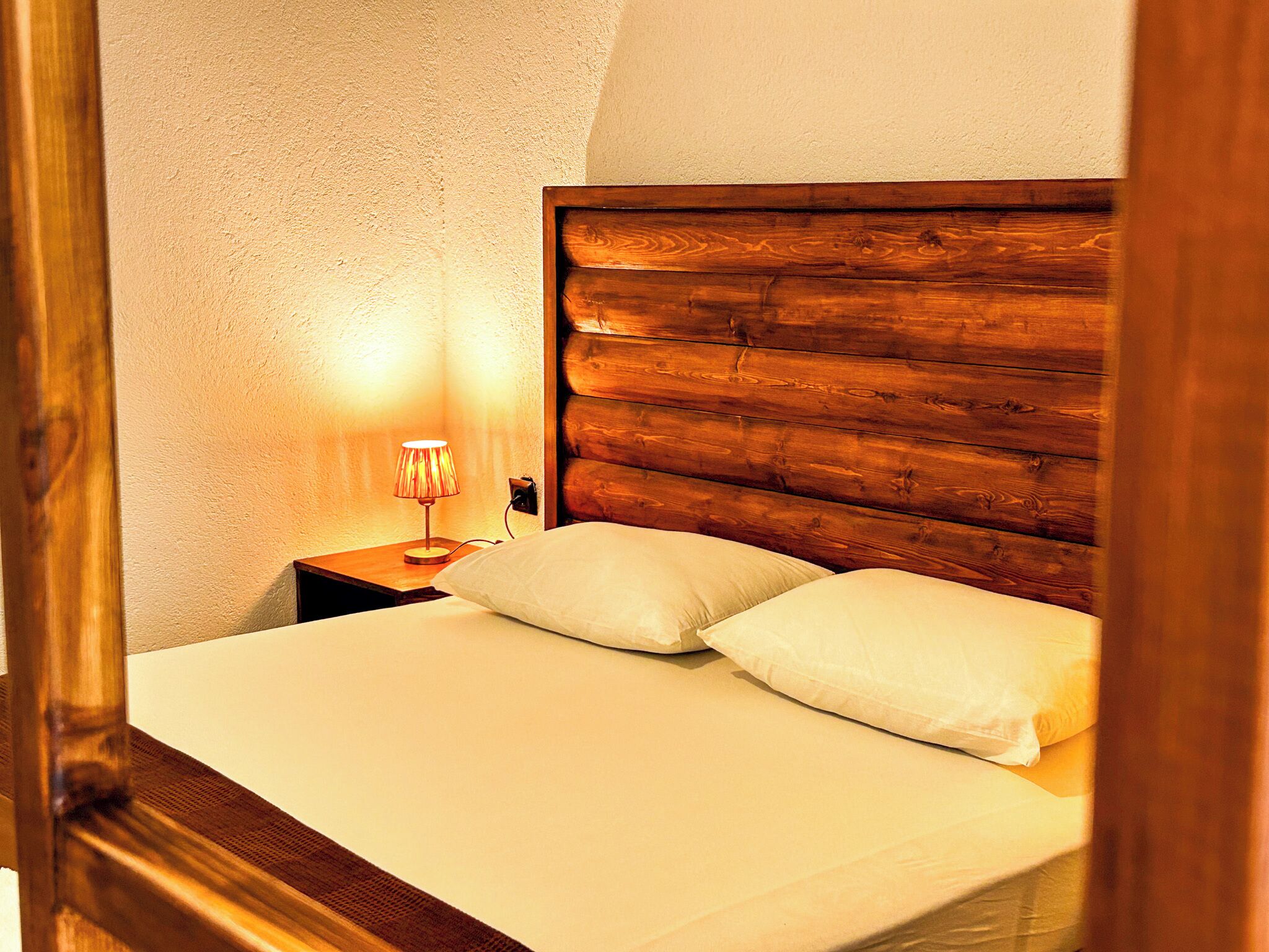 A neatly made bed with a wooden headboard, a bedside lamp, and a white pillow.